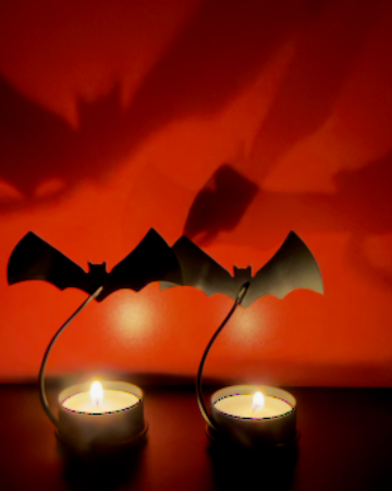 A set of 2 Halloween-themed bat-shaped tealight candle holders with two lit candles, casting a dramatic shadow of flying bats on a red wall background.