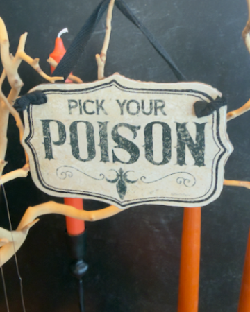 This set of two Halloween ornaments features two decorative hanging signs that reads 'PICK YOUR POISON' in distressed black lettering on an off-white background, suspended by a black ribbon.