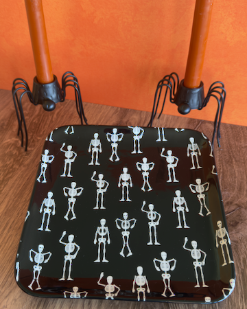 A square ceramic black appetizer tray with rounded corners, featuring a repeating pattern of small white stick-figure skeletons. Approx. 8.25" square.