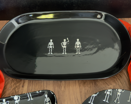 A large ceramic glossy black oval serving platter with three small silver skeleton figurines arranged in a row at the center. approx. 20" x 10"