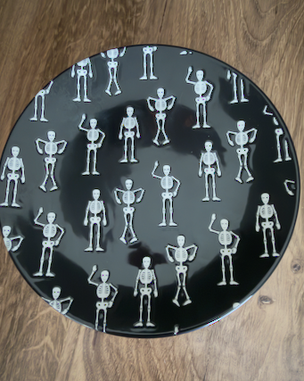 This quirky, fun Halloween Salad Plate is a round black ceramic plate with a repeating white pattern of small dancing skeletons. Approx. 8.5" round.